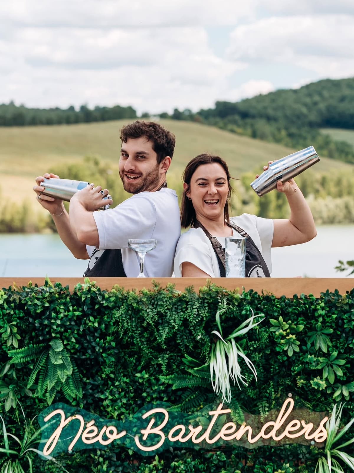 Titouan et Maëva dos à dos, shakers levés, derrière leur bar Néo Bartenders